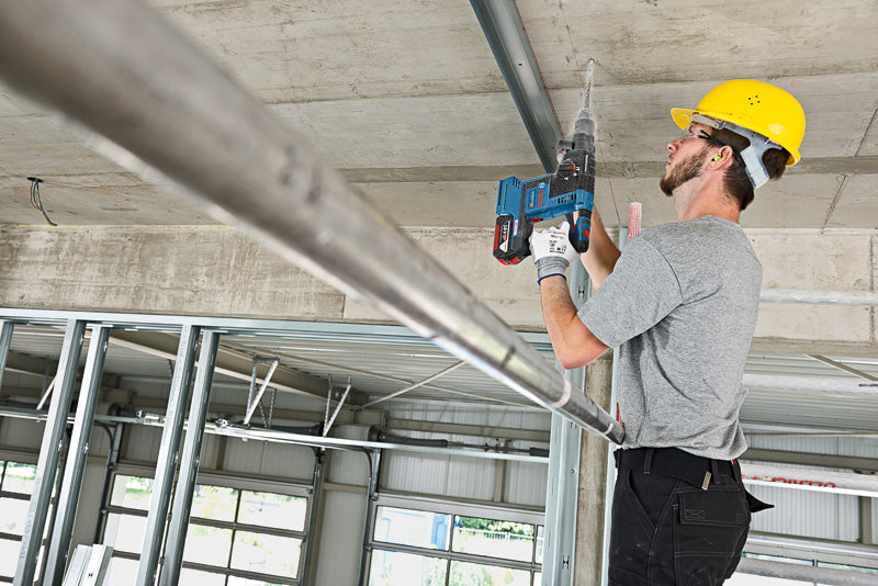 Eine Person mit Sicherheitsausrüstung bohrt auf einer Baustelle in eine Decke.