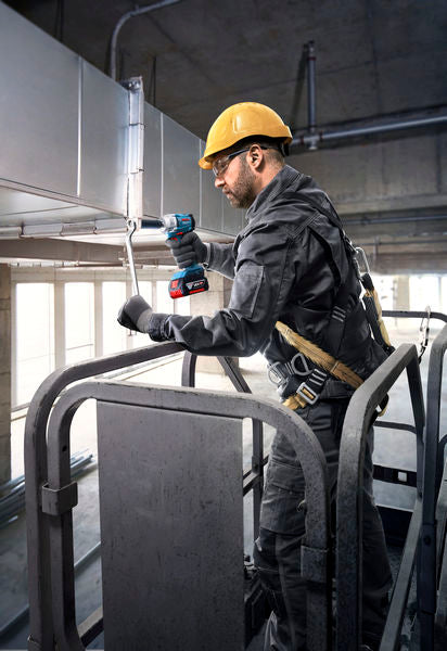 Eine Person mit Sicherheitsausrüstung befestigt mit einem Akku-Elektrowerkzeug Rohrleitungen.