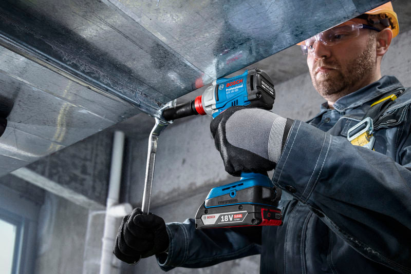 Eine Person mit Sicherheitsausrüstung befestigt mit einer Akku-Bohrmaschine einen Metallkanal.