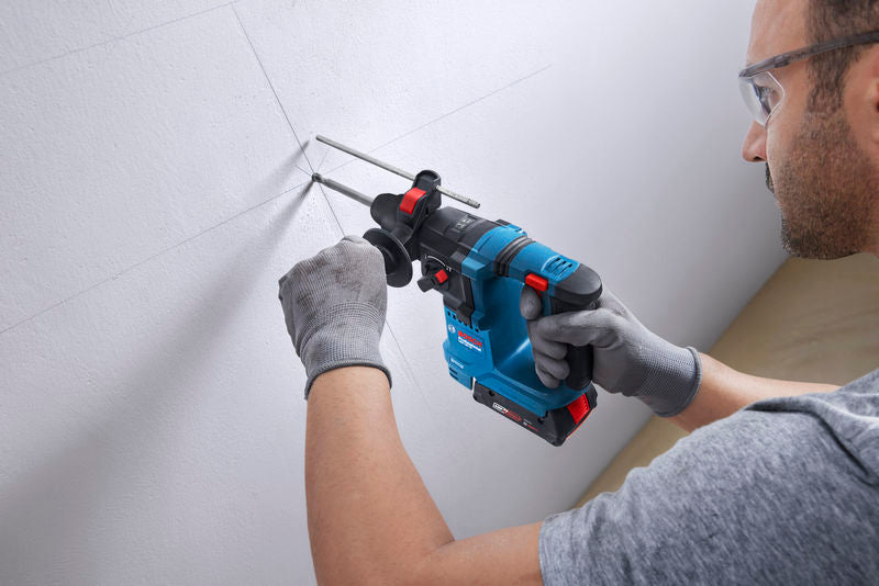 Eine Person mit Schutzausrüstung bohrt mit einem Bohrhammer in eine Wand.