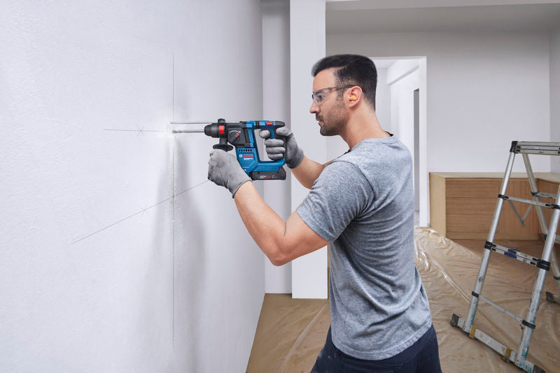 Eine Person mit Sicherheitsausrüstung bohrt ein Loch in eine markierte weiße Wand.