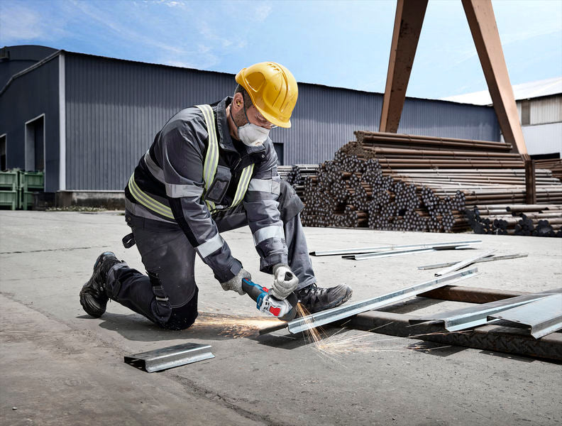 Eine Person mit Schutzausrüstung schleift im Freien Metallträger mit einem Winkelschleifer.