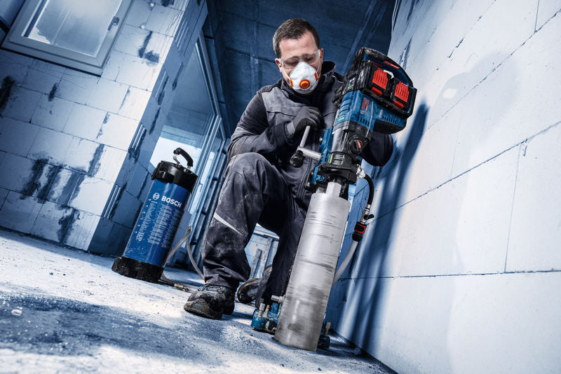 Eine Person mit Sicherheitsausrüstung bohrt mit einem Bosch Expert Diamantbohrer ein Loch in eine Betonwand