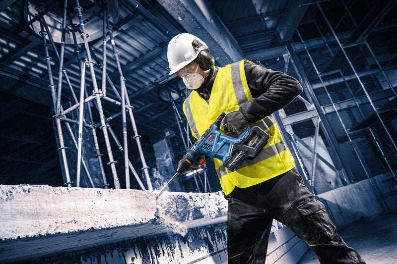 Eine Person mit Sicherheitsausrüstung bohrt auf einer Baustelle in Beton