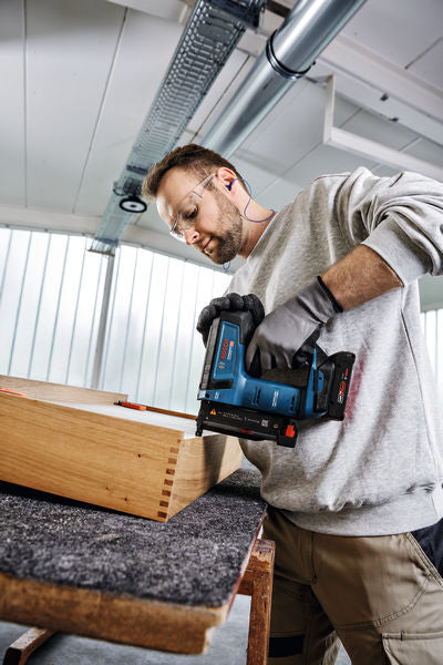 Eine Person mit Sicherheitsausrüstung befestigt Holzverbindungen mit einem Akku-Nagler.