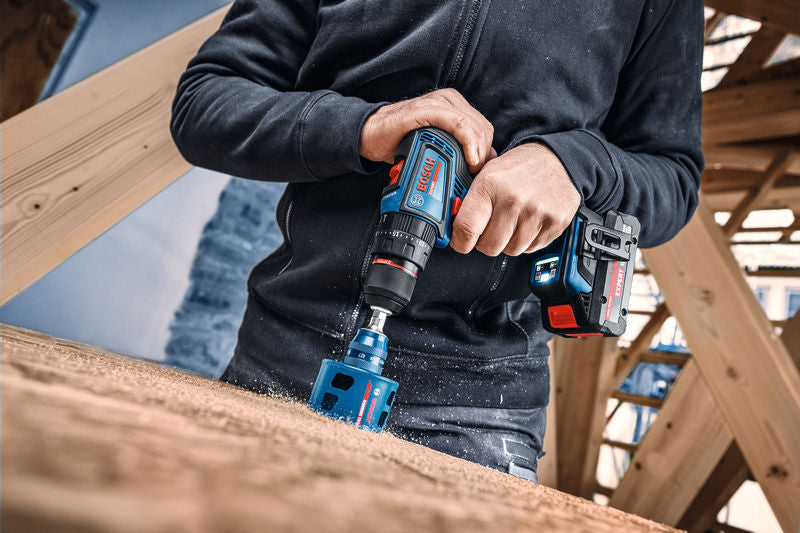 Auf einer Baustelle bohrt eine Person mit einem Akku-Kombigerät ein großes Loch in Holz