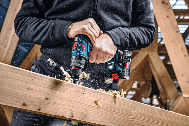 Eine Person bohrt mit einem Akku-Kombigerät in einen Holzbalken