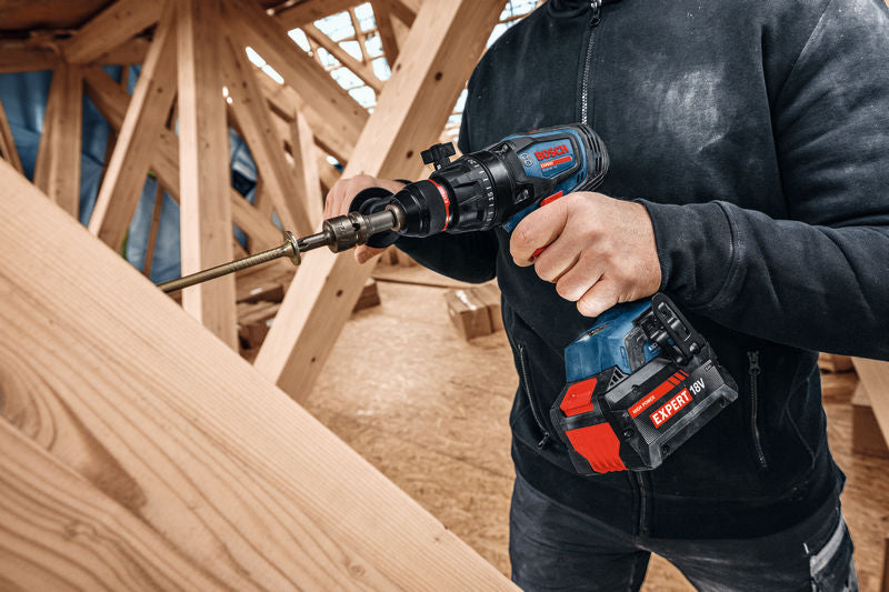 Eine Person schraubt mit einem Akku-Schlagbohrschrauber eine große Schraube in Holz