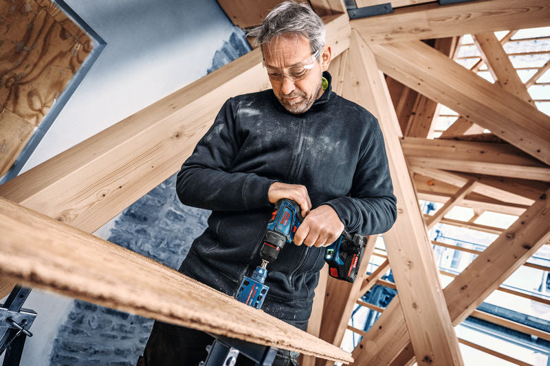 Eine Person mit Schutzausrüstung bohrt mit einem Akkubohrer in Holz