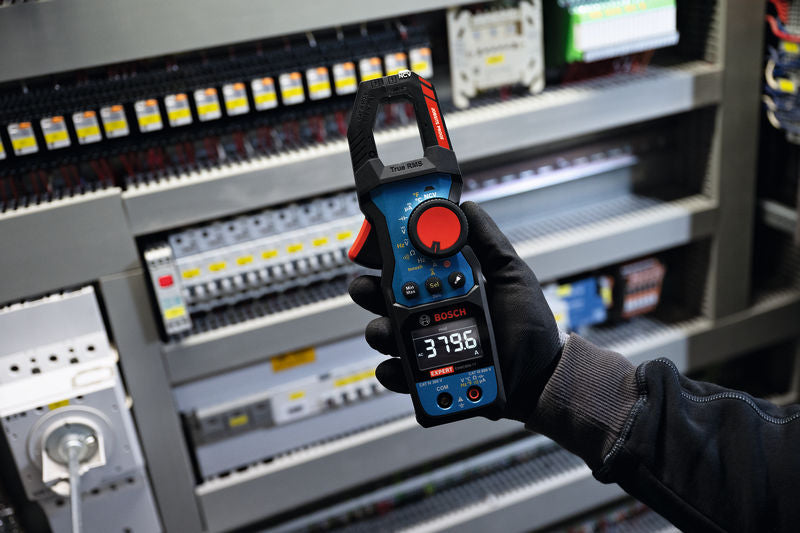 Eine Person mit Sicherheitsausrüstung verwendet ein Zangenmessgerät vor einem Schaltschrank