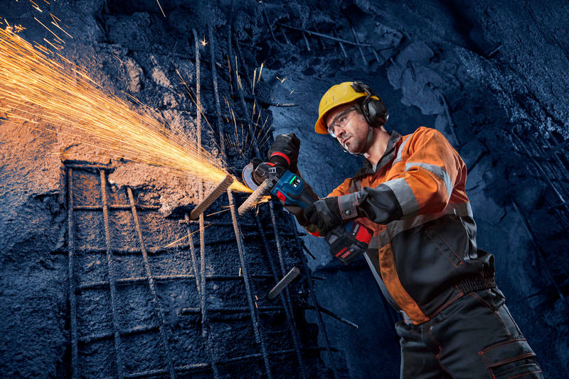 Eine Person mit Schutzausrüstung schneidet mit einem Winkelschleifer Metallstangen, wobei Funken entstehen