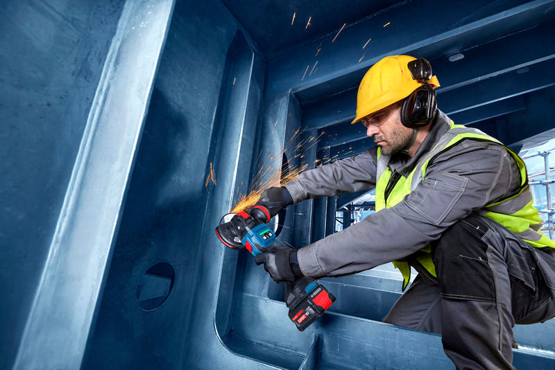 Eine Person mit Schutzausrüstung verwendet einen Akku-Winkelschleifer an einer Stahlkonstruktion