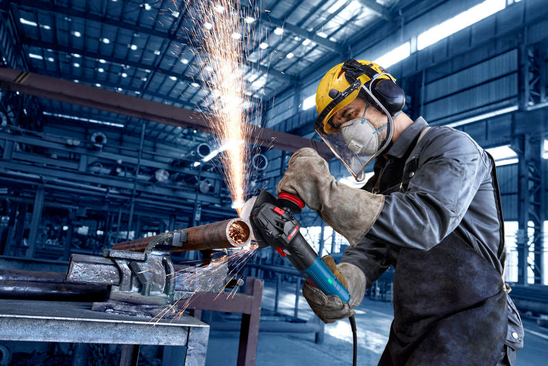 Eine Person mit Sicherheitsausrüstung schleift in einer Fabrik ein Metallrohr und erzeugt dabei Funken