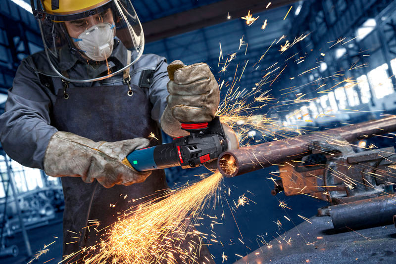 Eine Person mit Sicherheitsausrüstung schleift in einer Industriewerkstatt ein Metallrohr