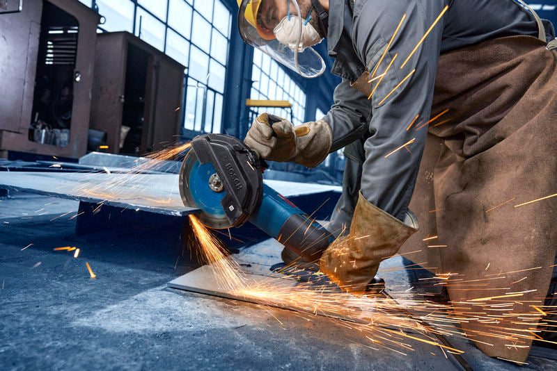 Eine Person mit Schutzausrüstung schleift Metall mit einem Winkelschleifer, wobei Funken entstehen.