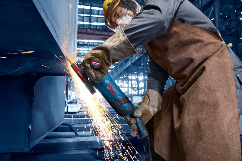 Eine Person mit Schutzausrüstung schleift Metall und erzeugt dabei einen Funkenregen