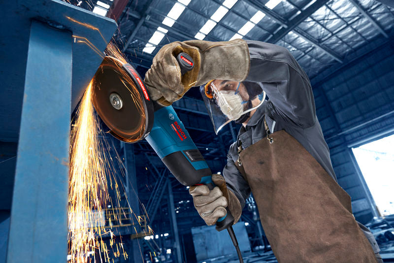 Eine Person mit Sicherheitsausrüstung schleift in einer Industriewerkstatt Metall und erzeugt dabei Funken