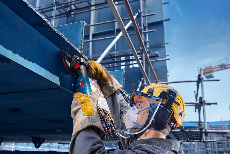 Eine Person mit Sicherheitsausrüstung schleift auf einer Baustelle Metallträger