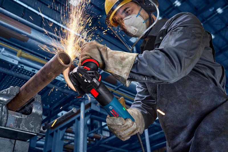 Eine Person mit Sicherheitsausrüstung schleift ein Metallrohr, wodurch Funken entstehen.