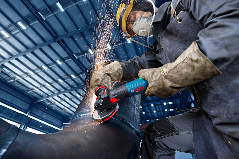 Eine Person mit Schutzausrüstung schleift mit einem Winkelschleifer ein Metallrohr