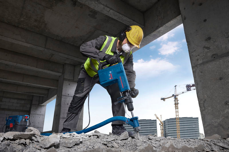 Eine Person in Schutzausrüstung sprengt Beton mit einem Abbruchhammer.