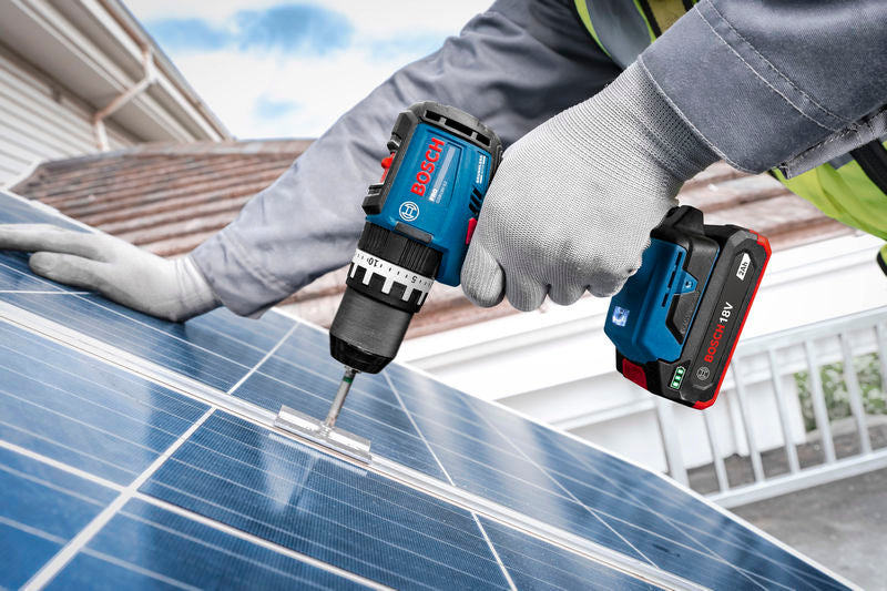 Eine Person, die Schutzausrüstung trägt, befestigt mit Hilfe eines Akku-Schlagbohrers eine Halterung an einem Solarpanel.