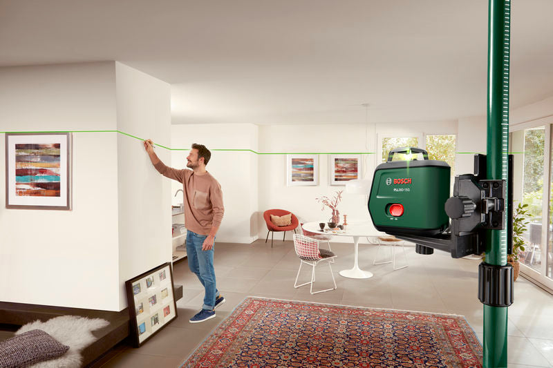 Eine Person markiert eine Wand mithilfe eines Laser-Nivelliergeräts, das eine grüne Linie projiziert.