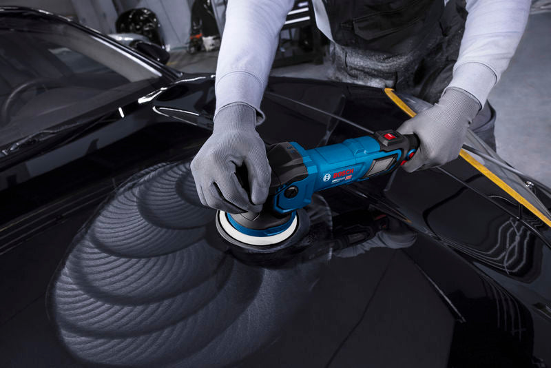 Eine Person in Schutzausrüstung poliert eine Motorhaube mit einer blauen Poliermaschine.