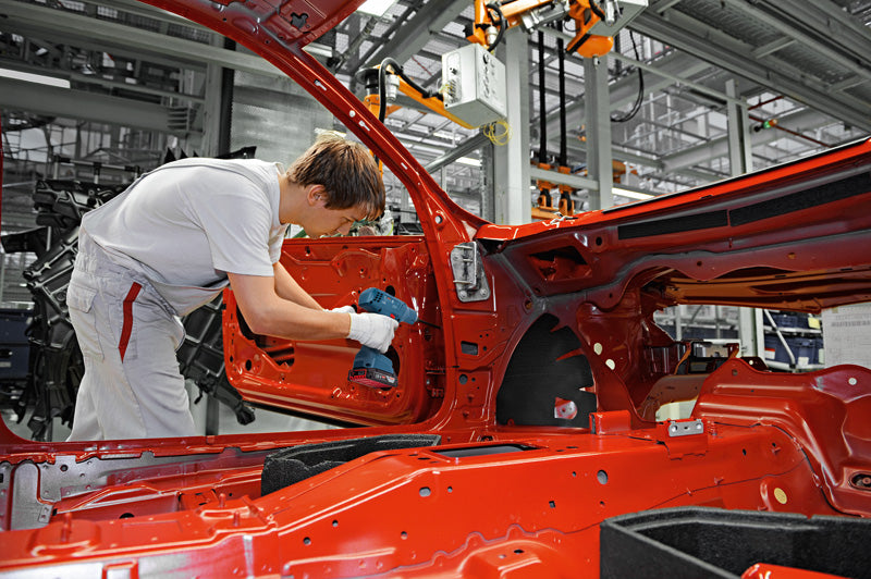 Eine Person mit Sicherheitsausrüstung montiert in einer Fabrik mit einer Akkubohrmaschine eine Autotür.