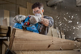 Eine Person mit Schutzausrüstung glättet einen großen Holzbalken mit einem Elektrohobel.
