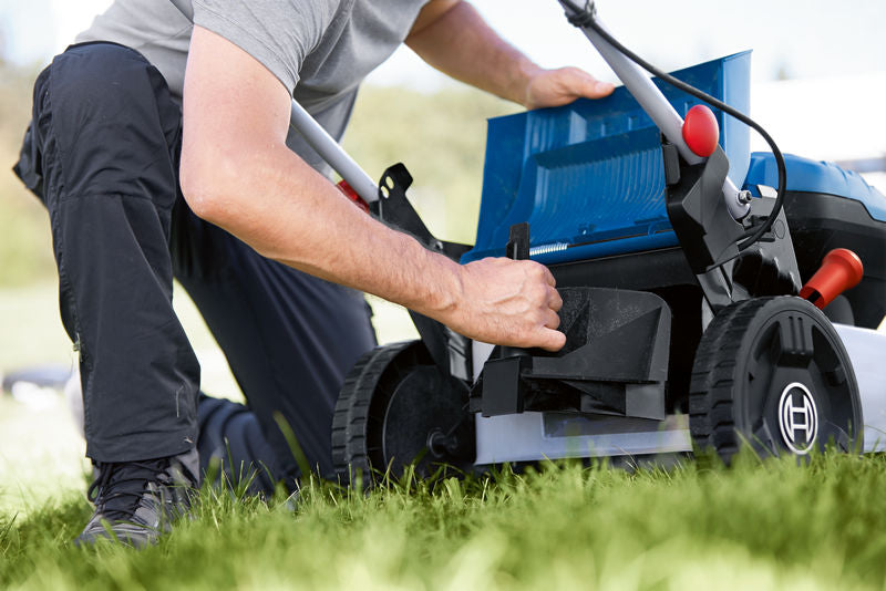 Eine Person stellt das Fach eines Akku-Rasenmähers auf einer Rasenfläche ein.