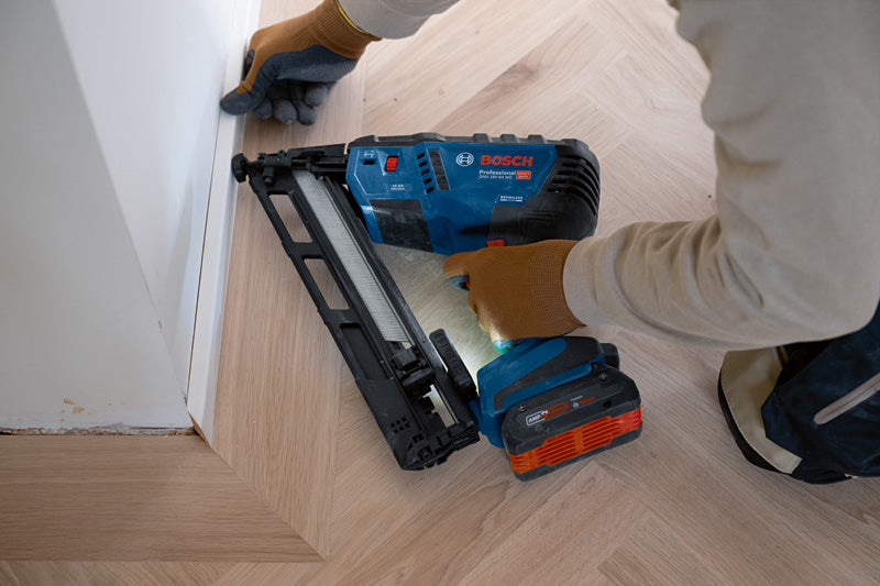 Eine Person mit Sicherheitsausrüstung befestigt mit einem Akku-Holznagler Zierleisten auf einem Holzboden.
