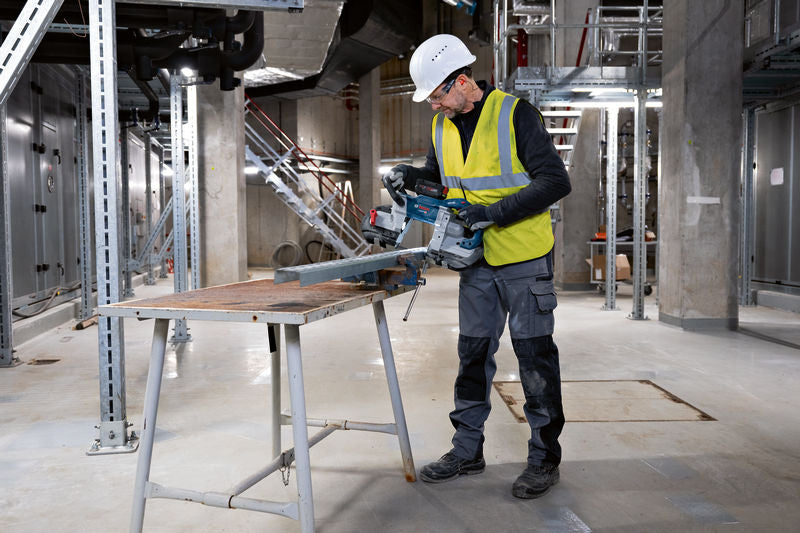 Eine Person mit Schutzausrüstung schneidet einen Metallträger mit einer Akku-Bandsäge.