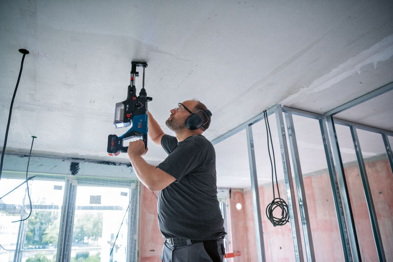Eine Person mit Schutzausrüstung bohrt mit einem Akku-Bohrhammer in eine Decke.