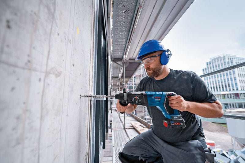 Eine Person mit Schutzausrüstung bohrt mit einem Bohrhammer in eine Betonwand.