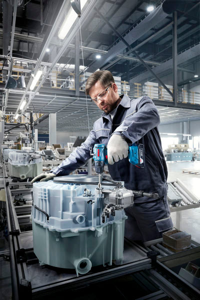 Eine Person mit Sicherheitsausrüstung montiert in einer Fabrik Maschinen mit einer Akkubohrmaschine.