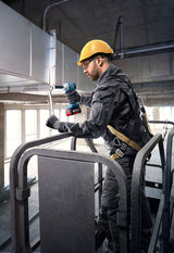 Eine Person mit Sicherheitsausrüstung befestigt mit einem Akku-Elektrowerkzeug Rohrleitungen.
