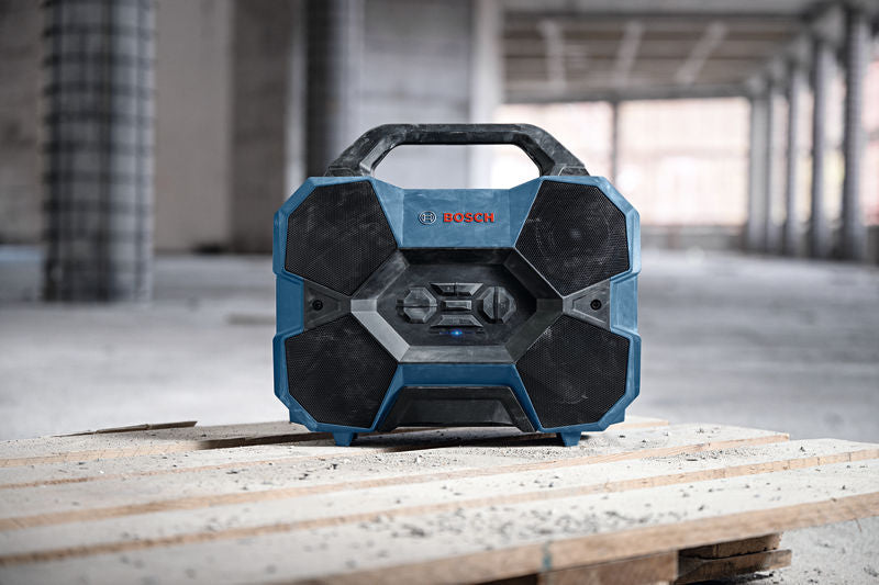 Baustellenradio mit robustem Design steht auf Holzbrettern auf einer Baustelle.