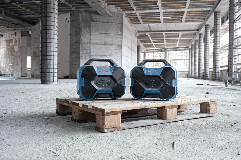 Zwei robuste Radios auf einer Holzpalette in einem großen, unfertigen Gebäude.