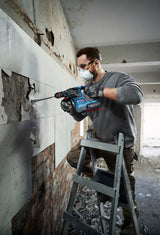 Eine Person mit Schutzausrüstung entfernt Wandfliesen mit einem Bohrhammer.