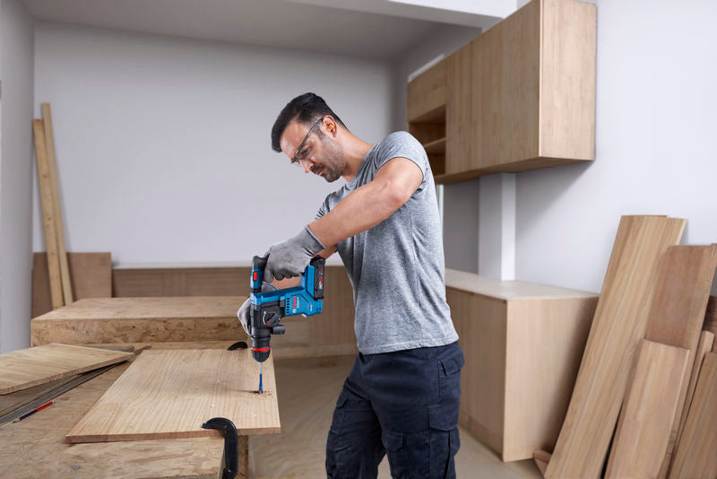 Eine Person mit Schutzausrüstung bohrt mit einem Akku-Bohrhammer in Holz.