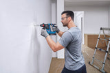 Eine Person mit Sicherheitsausrüstung bohrt ein Loch in eine markierte weiße Wand.