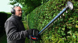 Eine Person mit Schutzausrüstung schneidet eine Hecke mit einer Akku-Heckenschere.