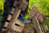 Eine Person mit Sicherheitsausrüstung schneidet Holzbretter mit einer Akku-Gartensäge.