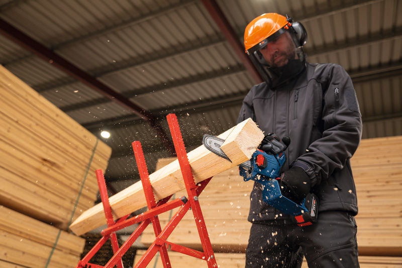 Eine Person mit Sicherheitsausrüstung schneidet im Innenbereich mit einer Akku-Hochentastersäge Holz.