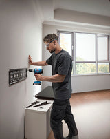 Eine Person mit Sicherheitsausrüstung installiert mit einer Akkubohrmaschine eine Metallhalterung an einer Wand.