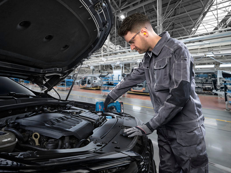 Eine Person mit Sicherheitsausrüstung verwendet in einer Fabrik ein Akkuwerkzeug an einem Automotor.