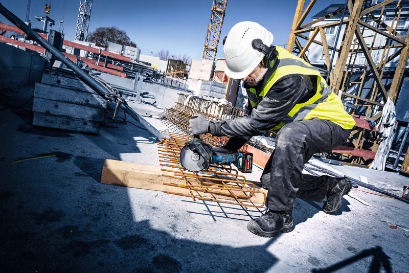Eine Person mit Sicherheitsausrüstung schneidet auf einer Baustelle Bewehrungsstahl mit einem Akku-Winkelschleifer