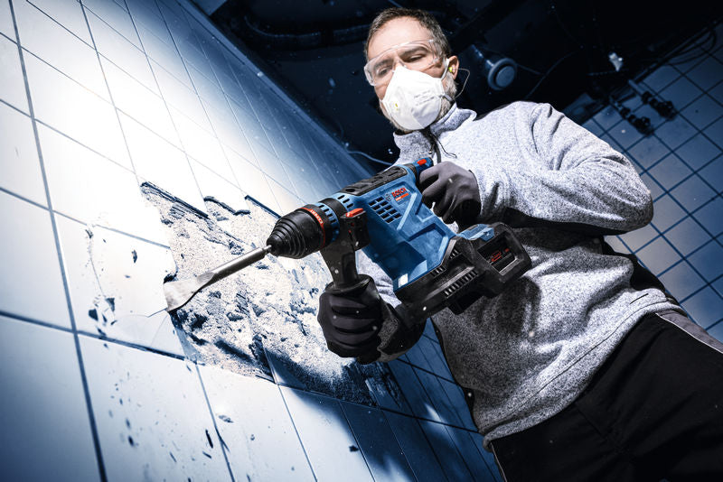 Eine Person mit Schutzausrüstung bohrt mit einem Akku-Bohrhammer in eine geflieste wand