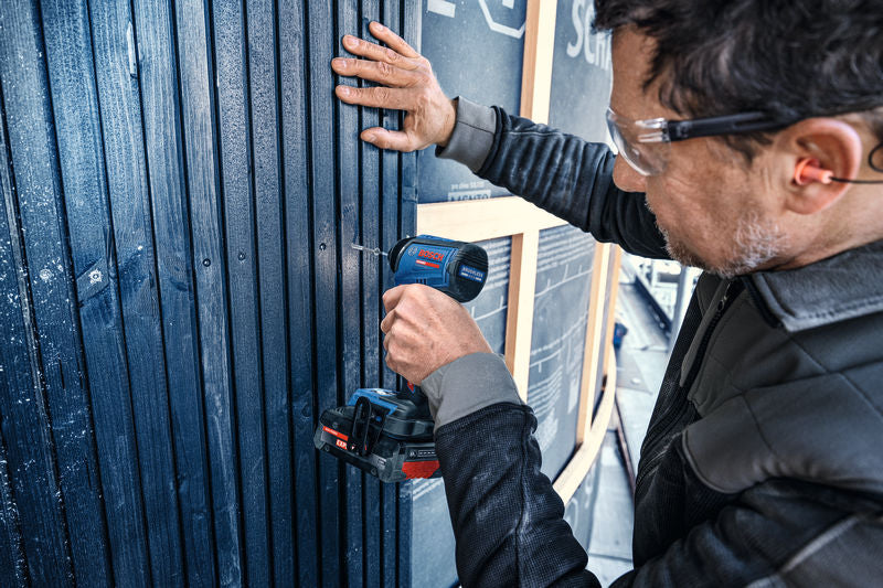 Eine Person mit Schutzausrüstung bohrt mit einem Schlagschrauber in eine Holzwand